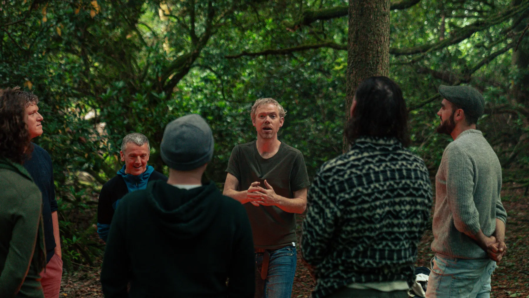 Niall speaking with a circle of men in the woods